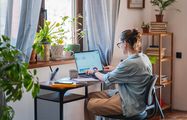 Young female freelancer working learning from home at home using laptop with chart on screen....
