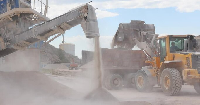 Stone crushing machine at open pit mining and processing plant for crushed stone and loader with truck. Piles of gravel stone and conveyor belts on the side of the road