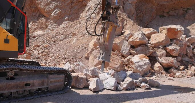Excavator with hydraulic hammer breaking rock. Stone crushing machine at open pit mining and processing plant for crushed stone, slow motion. Concepts of industry and building materials