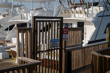 Gate entrance to a private marina dock with fishing boats, with signs for no trespassing.
