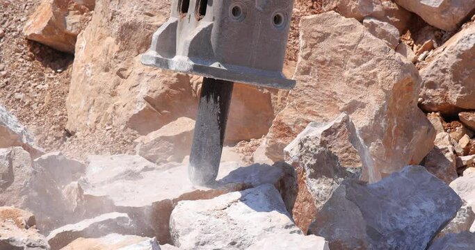 Excavator with hydraulic hammer breaking rock. Stone crushing machine at open pit mining and processing plant for crushed stone, slow motion. Concepts of industry and building materials