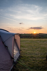 Sunset on campsite with tent in the foreground in grass meadow