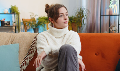 Sad lonely young woman sitting at home room looks pensive thinks over life concerns or unrequited...