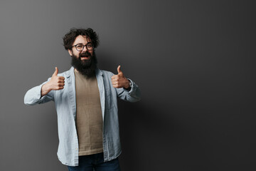 Cheerful happy bearded man wearing eyeglasses showing thumbs up over black background, studio shot