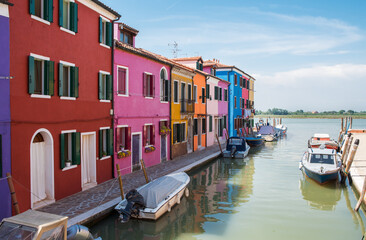 Fototapeta na wymiar Colorful houses along the canal with parked boats on Burano island, Venice, Italy. Attractive famous travel destination.