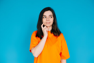 Attractive Young Woman in Trendy Orange Clothes, Pensive and Skeptical Expression, Empty Space for Copy, Isolated on Blue Background - Portrait Photo