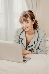 Freelancer woman pajamas, she lies in bed and uses work on laptop, computer, study on the Internet, surf the internet, relax, relax, spend time in the bedroom, living room, at home, in the hotel room