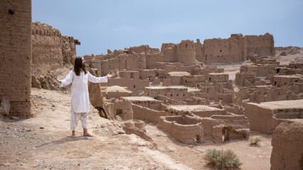 man in white robes standing with arms open in front of a ancient city ruins in desert