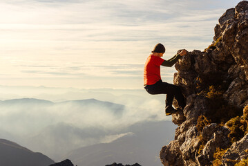 male climber in red clothes climbing a rock without a rope or safety measures to reach the top of a...