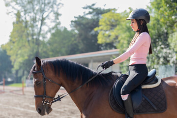 Close up of a young woman riding a horse in an equestrian center, while taking riding lessons