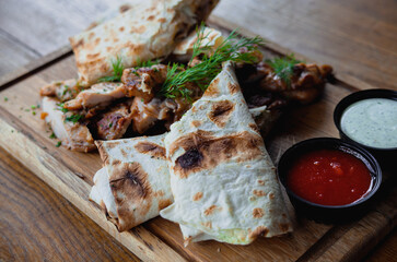 Shawarma chicken roll in a pita with fresh vegetables, cream sauce and french fries on wooden background. Selective focus