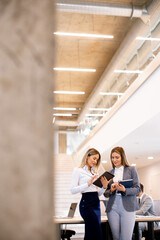 Two young business women looking at financial results on digital tablet in front of their team at...