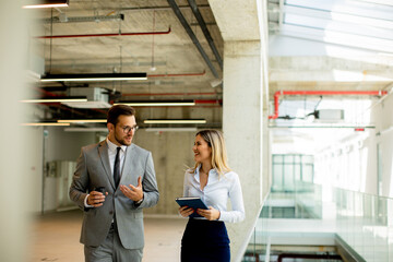 Young coworkers walking and talking along corridor in modern office