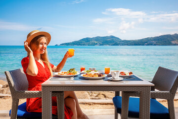 Woman enjoys breakfast with sea view at luxury hotel resort on tropical beach. Beautiful girl...
