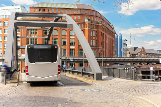 Back view of municipal public transport electric bus driving on paved road Elbe metal bridge in Hamburg old city center hafencity Germany. People commute E-bus traffic transport in Europe town