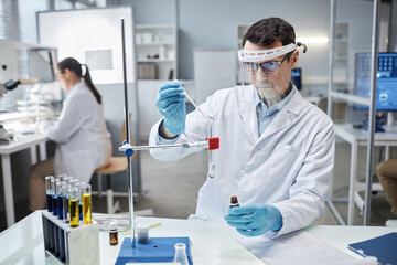 Waist up portrait of male scientist wearing face shield in laboratory while doing experiments with...