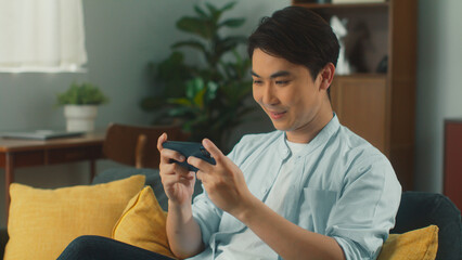 Happy attractive young Asian man hand holding smartphone focus on and enjoy playing MOBA MMORPG...