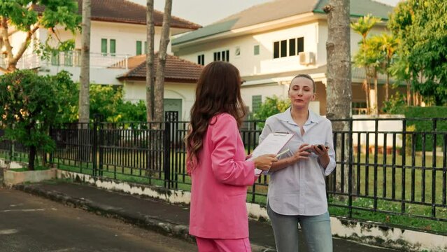 n an upscale residential area, a realtor and her client are conversing and joke while standing in front of houses