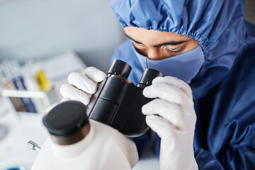 Closeup of scientist looking in microscope while wearing protective gear in laboratory, copy space
