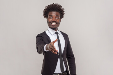 Friendly man with petit goatee, giving hand for handshake as sign of greeting, smiling widely and...