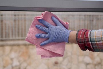 Woman hand in blue gloves cleaning glass railing in patio with pink rag.Housework concept. Closeup photo.