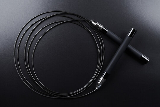 Black fitness skipping rope close-up on black background. Crossfit sports equipment