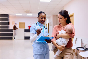Happy mother with baby talks to pediatric nurse at medical clinic.