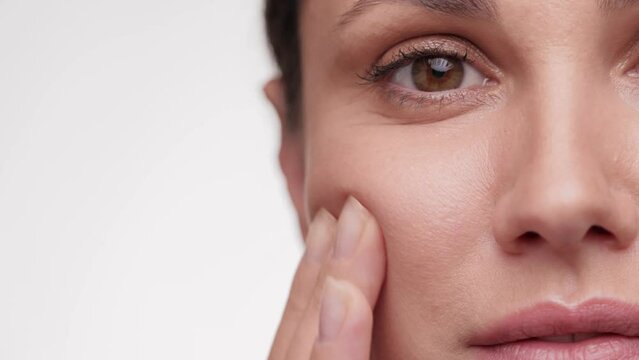 View half face of beautiful female face. Concept for fresh moisturized elasticity skin. Brunette woman massaging and touching her face after applying cream. Natural healthy face. slow motion.