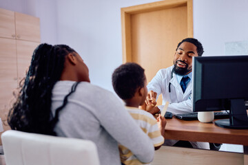 Happy black pediatrician examining small boy at doctor's office.