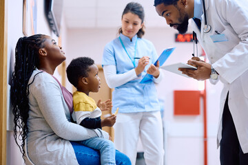 Black mother and son talk to pediatrician in waiting room at medical clinic.