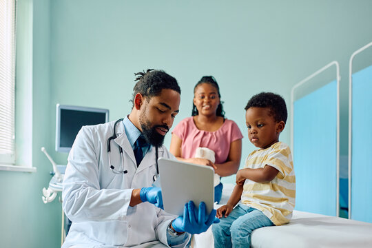 Black kid and his pediatrician using digital tablet at doctor's office.