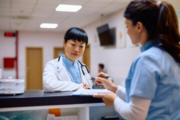 Japanese female doctor communicating with nurse at reception desk in hospital.