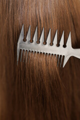 Fototapeta premium Close up of haircare, comb moves along beautiful healthy long flowing brown hair, texture. Healthy long smooth flowing brown hair