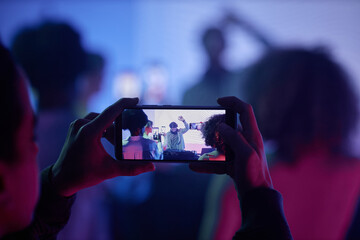 Closeup of man filming DJ at disco party via smartphone, focus on smartphone screen, copy space