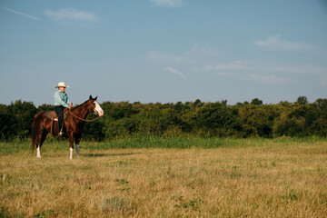 Western lifestyle with senior woman cowgirl riding horse in Texas summer pasture outdoors.