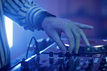 Side view closeup of male DJ adjusting switches at turntable in neon lights at disco party, copy space