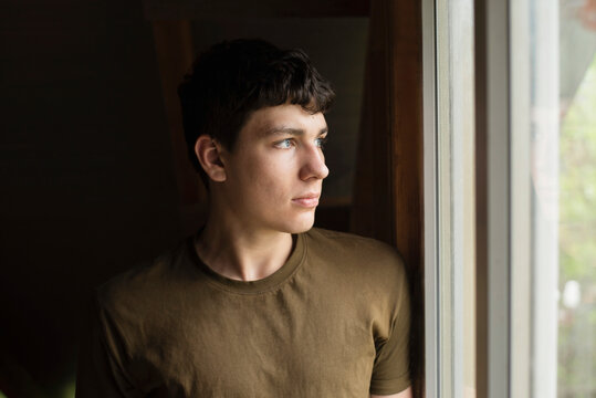 Standing in front of the window and thinking, a young 18-year-old dreams, chooses whether to study or work. Portrait of a charismatic serious guy