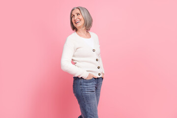 Profile portrait of positive friendly aged lady put hands pockets look empty space toothy smile isolated on pink color background