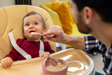Baby eating her dinner with dad, unrecognizable father feeding toddler kid.