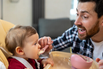 Baby eating her dinner with dad, father feeding toddler kid.