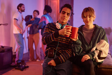 Portrait of retro styled young couple at house party holding red cups and looking at camera, copy...