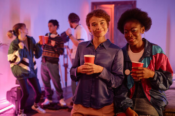 Portrait of two girls at retro house party holding red cups and looking at camera, copy space