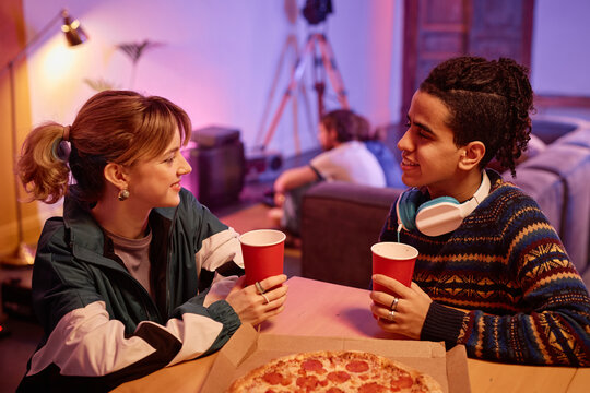 Side view portrait of young couple eating pizza and chatting at retro house party