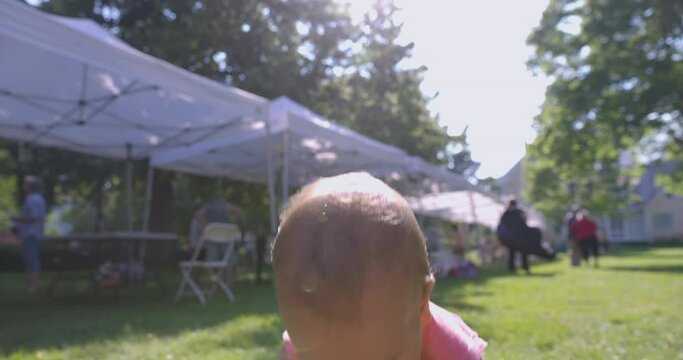 Toddler girl playing outdoors at summer fair looks down at lawn - close up on face