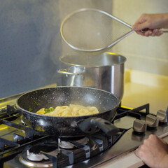 Image of the hands of a woman who drains the pasta in the kitchen. Woman preparing lunch.
