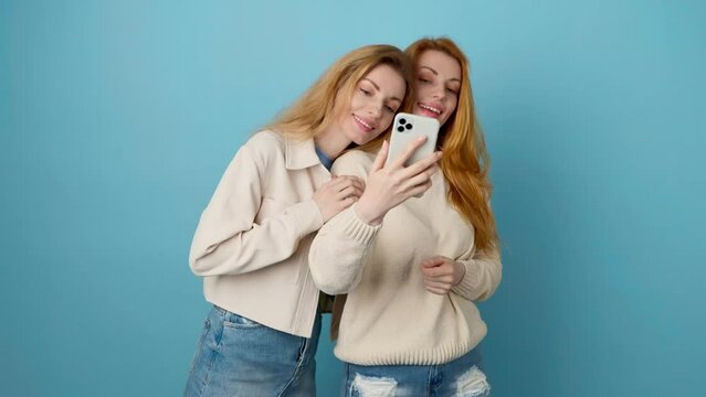 Selfie, friends, and woman posing with phone, peace sign for social media post. Two women sister, fashionable with mobile smartphone friendly smiling, taking profile picture, studio blue background