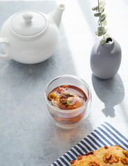 A cup of herbal tea, teapot and homemade cookies on a blue background with morning shadow. Drink concept for breakfast.