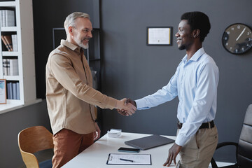 Side view portrait of smiling senior candidate shaking hands with recruiter at job interview