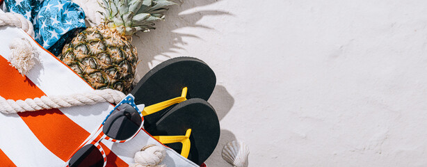 beach bag with pineapple sunglasses and swimsuit on white sand on the beach