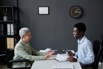 Side view portrait of smiling senior woman with disability speaking to HR recruiter in job interview
